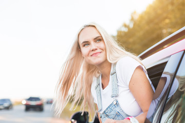 Fototapeta na wymiar Young pretty woman driving car and leaning out of car window. traveling by car, summer holidays