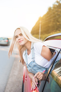 Young pretty woman driving car and leaning out of car window. traveling by car, summer holidays