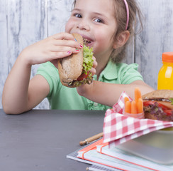 The schoolgirl holds a lunch and books for study on the table near the board. Free space for text. Healthy food for the baby