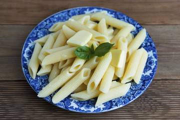 Cooked penne pasta with butter and cheese and basil in vintage beautiful blue plate on wooden table. Isolated.