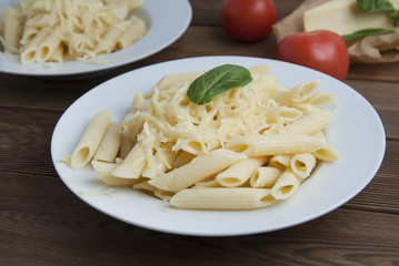 Cooked penne pasta with butter and cheese, isolated in white round plate, over wooden table, decorated with basil leaves. Top view. Clasic italian pasta.