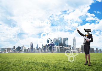 Camera headed woman standing on green grass against modern cityscape