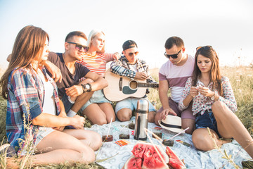 Happy young friends having picnic in the park.They are all happy,having fun,smiling and playing guitar.