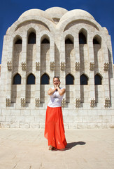 young attractive happy sunny girl in white blouse, long orange skirt and sunglasses is standing like model and posing near white stone church with columns background in Egypt and smiling