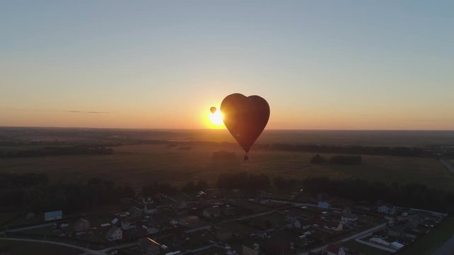 Aerial view Hot air balloon shape heart in sky over field in countryside, beautiful sky and sunset. Aerostat fly over countryside.Aerial footage 4K