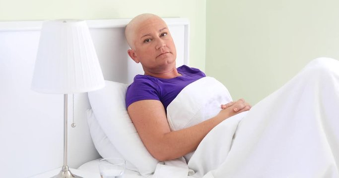Bored female cancer patient laying in bed, looking at the camera