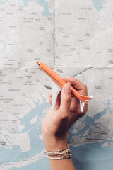 partial view of woman holding toy plane in hand with map on background, vacation concept