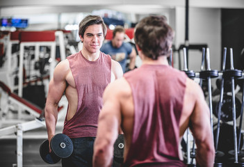 Fototapeta premium Muscular handsome man with dumbbells in gym