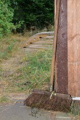 Alter Reisigbesen vor einem Holztor mit Blick in einen Garten im Sommer