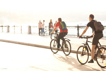 two guys ride on bicycles on the sunny city embankment - Powered by Adobe