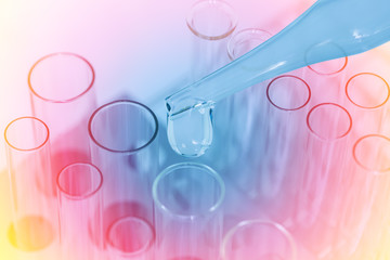 Close up the emerging drop of chemical solution from a dropper over laboratory a pile of test tubes in test tube rack, science background
