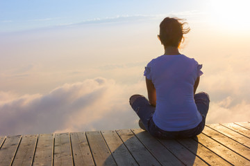 A young woman is sitting on a wooden platform at sunset high in the mountains of Sochi, Russia, 08/22/2017
