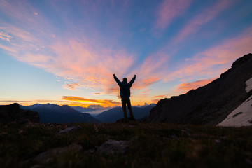 Man standing on mountain top outstretching arms, sunrise light colorful sky scenis landscape,...
