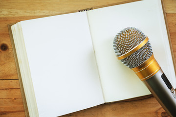 Microphone on an opened notebook on wooden background for speaking, learning and teaching concept