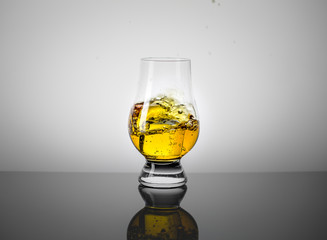 Taster Glass with a Dram of Scotch Whisky and Ice Cube Falling into it.