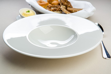 Table settings. Empty plate, with spoon, butter dish and basket with bread