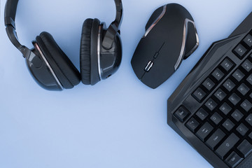 Headphones, mouse, keyboard on the blue background, top view. Gaming gear. Gamer workspace Gamer...