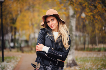 Fototapeta na wymiar fashion autumn portrait of young happy woman walking outdoor in fall park in hat and leather jacket