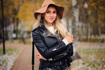 fashion autumn portrait of young happy woman walking outdoor in fall park in hat and leather jacket