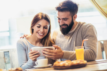 Smiling couple enjoying in pizza, having fun together and using tablet pc.