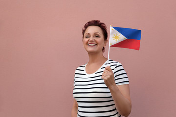 Obraz na płótnie Canvas Philippines flag. Woman holding Philippine flag. Nice portrait of middle aged lady 40 50 years old with a national flag over pink wall background outdoors.