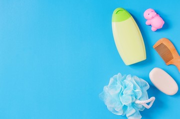 Flat lay photo toiletries/ Organic baby shampoo on a green packing, blue sponge puff, rubber toy hippo, wooden hair brush and soap bar. Flat lay beauty mockup. Top view still life photography