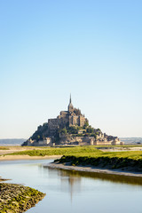 Fototapeta na wymiar View of the Mont Saint-Michel tidal island, located in France on the limit between Normandy and Brittany, at high tide with the Couesnon river in the foreground.