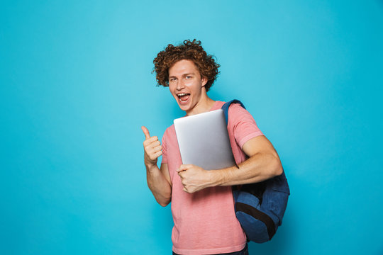 Photo of caucasian youngster guy with curly hair wearing casual clothing and backpack holding laptop, isolated over blue background