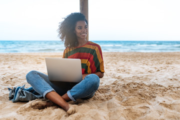 woman leaning on a straw umbrella at the beach with laptop