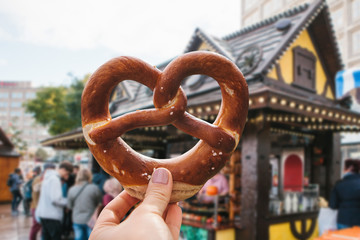 A girl or a young woman is holding a traditional German pretzel in the street. Oktoberfest festival...