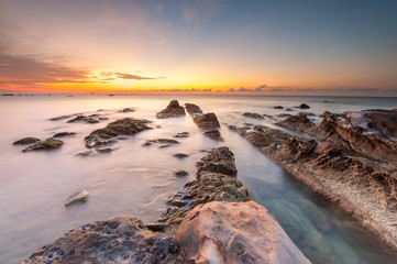 Sunset seascape with natural coastal boulders. beautiful sunset sky. soft focus due to slow shutter.