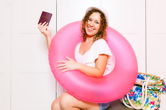 Woman sitting on luggage and holding a passport with inflatable round and ready for vacation trip. Preparing for the vacation concept