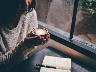 Woman holding a coffee cup and looking at the window in rainy day.