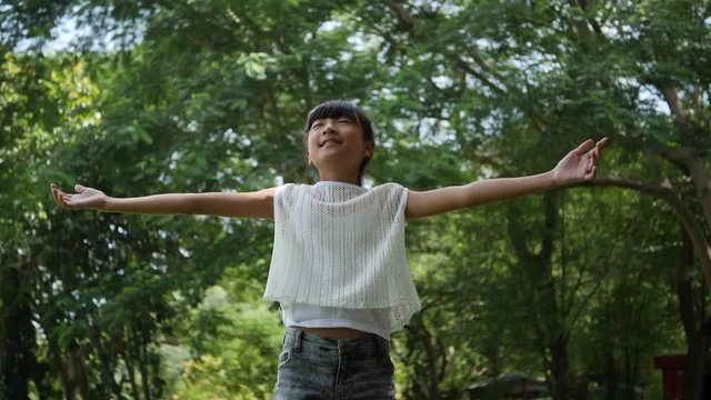 Asian little girl playing outdoor in slow motion, Spinning and smiling and raising hands in the air 