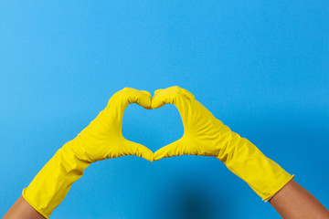 Hands in yellow rubber gloves making heart shape with fingers, on blue background
