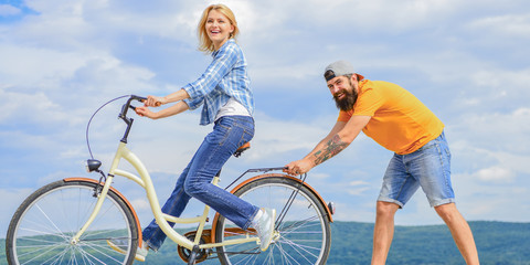 Teach adult to ride bike. Find balance. Woman rides bicycle sky background. How to learn to ride bike as an adult. Girl cycling while boyfriend support her. Man helps keep balance and ride bike