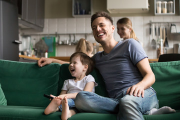 Happy dad and kid son holding remote control laughing at funny humor comedy film or tv show sitting...