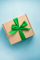 One craft paper box  with green ribbon bow on blue background from above. Minimalism, copy space