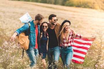 group of smiling young american travellers with flag walking by flower field