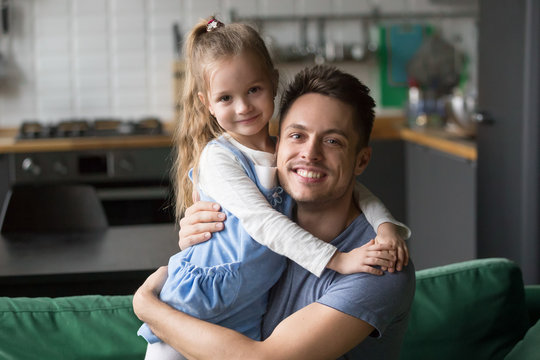 Portrait of happy dad hugging kid cute daughter looking at camera at home, smiling young daddy embracing cute girl expressing love and care, good single father posing with his child indoors concept