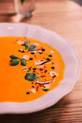Smooth pumpkin cream soup, white elegant plate, wooden table. Food photography concept. Close up