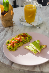 Spinach scrambled eggs with avocado toast on pastel pink plate. White marble table at the cafe. Sunny morning breakfast. Food photography concept