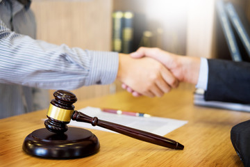 Gavel Justice hammer on wooden table with judge and client shaking hands after adviced in background at courtroom, lawyer service concept.