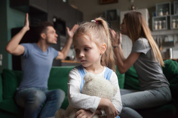 Kid daughter feels upset while parents fighting at background, sad little girl frustrated with psychological problem caused by mom and dad arguing, family conflicts or divorce impact on child concept - Powered by Adobe