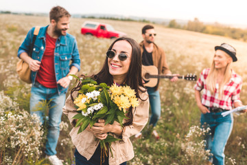 group of young people walking by field with guitar and flower bouquet