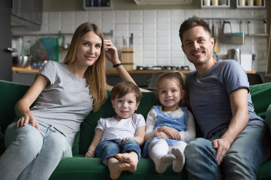 Portrait of happy parents with son and daughter sitting on comfortable sofa together, smiling loving family and cute kids looking at camera bonding on couch, children with mom and dad posing at home