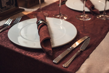 Empty plate with silver fork and knife on restaurant table with claret tablecloth