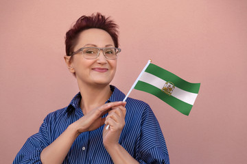 Andalusia flag. Woman holding Andalusian flag. Nice portrait of middle aged lady 40 50 years old with an autonomous flag over pink wall background. Visit Andalusia concept.