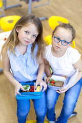two schoolgirls enjoying their healthy snack in the classroom at school