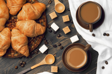 Two cups of coffee, croissants and sugar on a wooden background, top view